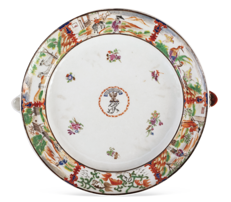 圖為清嘉慶廣彩描金花卉人物紋章溫盤，盤沿兩側(cè)對(duì)稱置半圓形注水口。外邊飾為鄉(xiāng)村風(fēng)景紋，盤心繪紋章，四周繪六組折枝花卉圍繞。溫盤又稱暖盤，使用時(shí)將熱水由孔注入，使盛入淺盤的食物保溫，達(dá)到防冷溫?zé)岬男Ч?。（?lái)源：廣州十三行博物館）